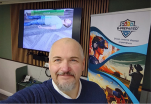 Selfie in a training room: smiling man, first aid training slide in the background, and a 'B-PREPARED' disaster preparedness banner.